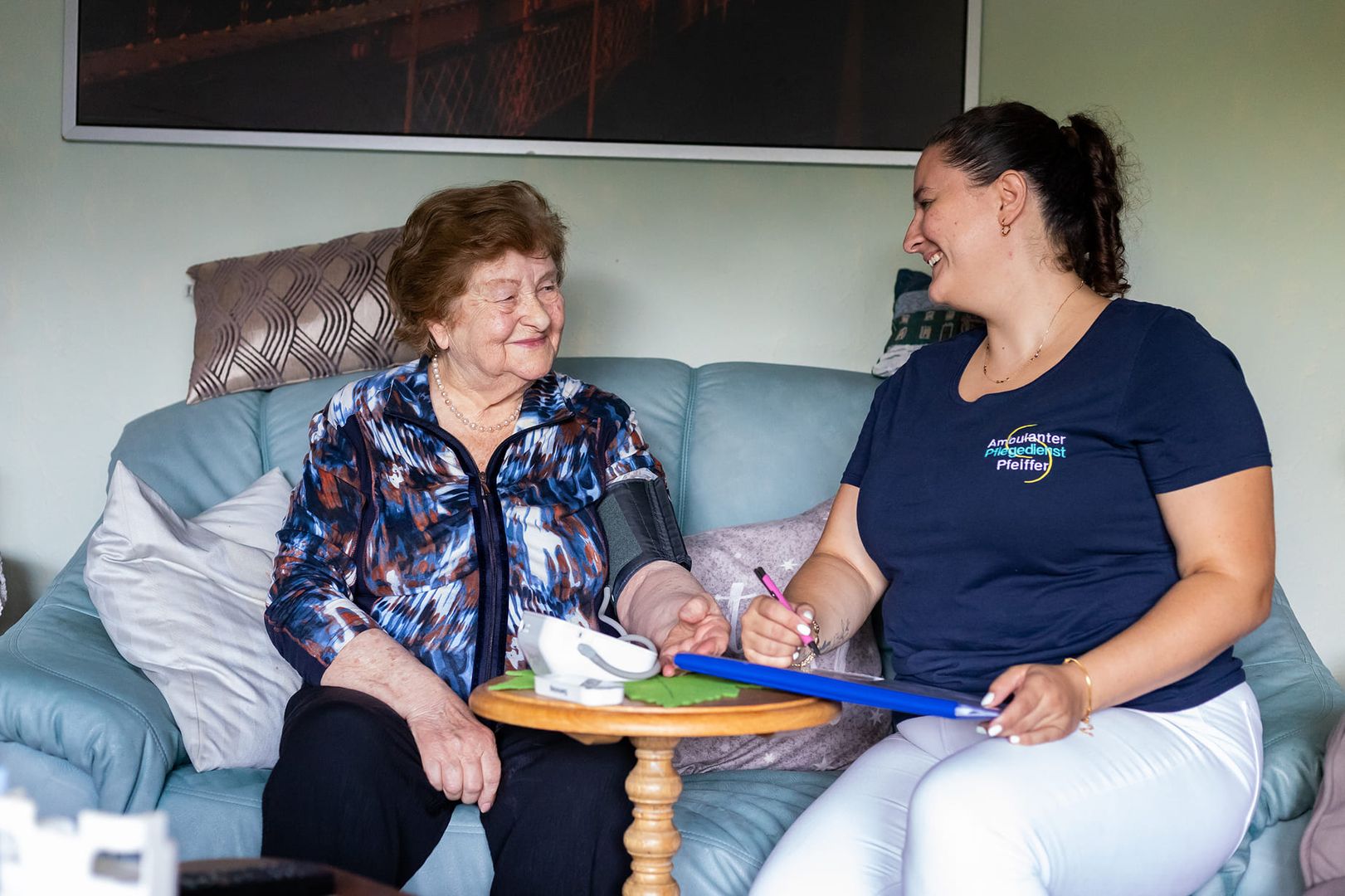 Eine Frau sitzt auf einem Sofa neben einer älteren Frau und sie unterhalten sich freundlich.